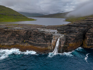 Beautiful aerial view of the Bøsdalafossur waterfall and Trælanípan magnificent landmarks in the Faroe Islands