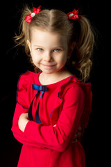 Cute blonde little girl standing on black backdrop