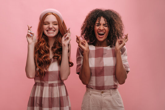 Two young interracial friends in plaid clothes with closed eyes, toothy smile and open mouth. European and African girls make wish and hope for best. Emotions and states of mind, concept