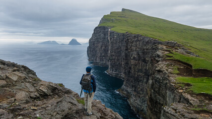 Beautiful aerial view of a tourist watching the Bøsdalafossur waterfall and Trælanípan magnificent landmarks in the Faroe Islands