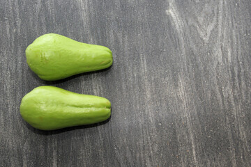 Fresh, raw and delicious freshly harvested chayotes and green squash ready to peel, chop and cook on a wooden table
