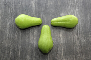 Fresh, raw and delicious freshly harvested chayotes and green squash ready to peel, chop and cook on a wooden table
