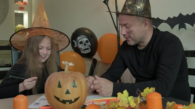 Child with father draw pictures on the theme of halloween in decorated room at home. Little girl and her dad laughing, smiling and having fun together, happy family preparing to celebrate the holiday.