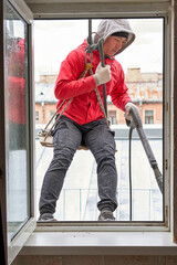 A window washer in climbing gear hangs in the window opening