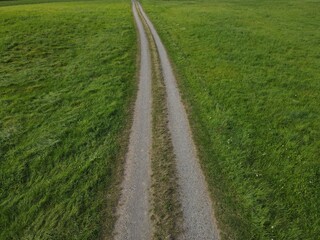Obraz premium Drone view of gravel road for agricultural vehicles between meadow