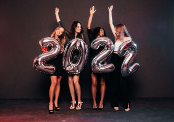 Beautiful Women Celebrating New Year.Happy Gorgeous Female In Stylish Sexy Party Dresses Holding Silver 2022 Balloons, Having Fun At New Year's Eve Party. Holiday Celebration.Charming Models