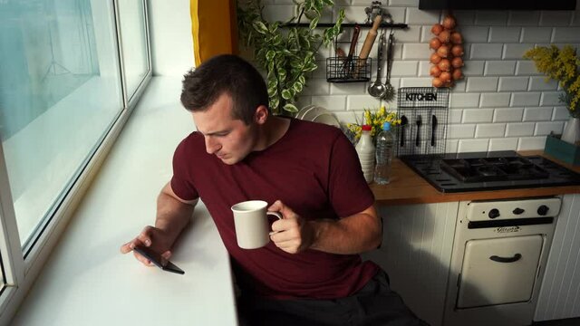 man drinks tea in the morning and simultaneously watches the news on the phone