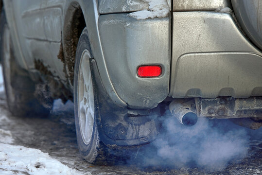 Car engine smoking, smoking exhaust pipe, closeup. Blue exhaust smoke. Car with gasoline or diesel  engine. Engine warming up at idle in winter season.