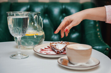 Closeup photo of female hands is reaching out to cake with cup of coffee in restaurant