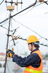 Male electrical worker or Asian man electrician wearing safety helmet and reflective suit repairing an old TV antenna and cable on rooftop of building.
