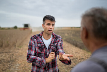 Two male farmers standing in harvested soy field talking.