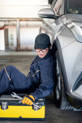 Fototapeta na wymiar Asian auto mechanic with tool box and wrench checking car wheel and tire in auto service garage. Mechanical maintenance engineer working in automotive industry. Automobile servicing and repair concept