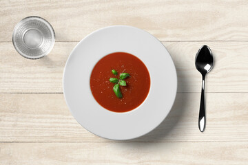 Tomato soup in white plate with spoon and water glass on wooden background