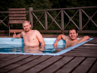 Two men relax in the pool against the background of the forest