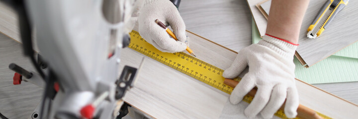 Young male repairman is markup wooden panel with pencil and ruler before cutting