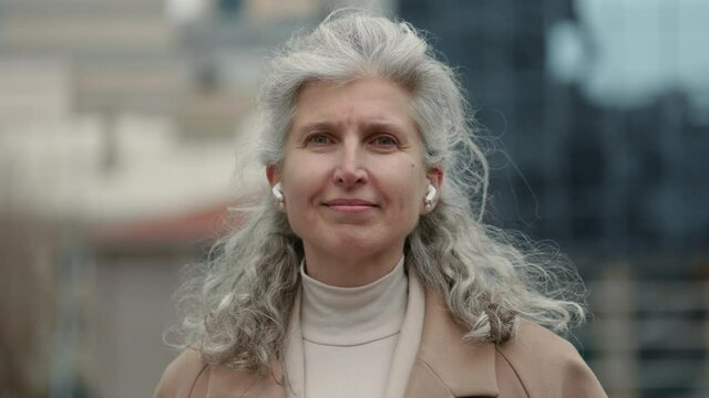 Aged female entrepreneur in earphones staning outdoors