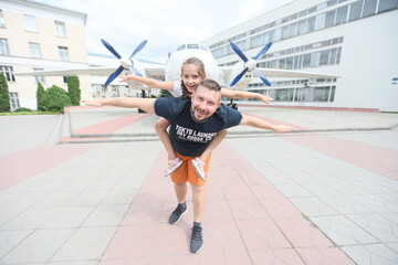 Happy dad and daughter are posing against the backdrop of a propeller plane on a city street.