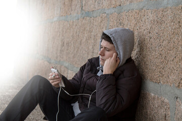 Fototapeta premium young man sitting in jacket and hat listening to music with the phone and headphones