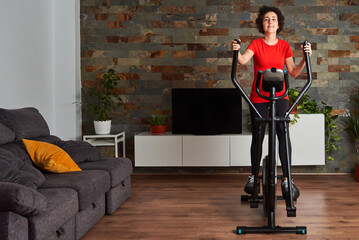 Fototapeta na wymiar Woman training at home using elliptical cross trainer