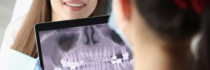 Dentist doctor examines X-ray picture on tablet screen in chair is woman patient - obrazy, fototapety, plakaty