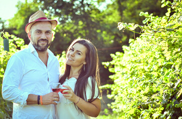 Portrait of a smiling  happy couple kissing    in a Vineyard toasting wine. Beautiful  brunette woman and bearded muscular man spending time together during grape harvest.
