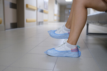 Women legs in sneakers with shoe covers in hospital corridor