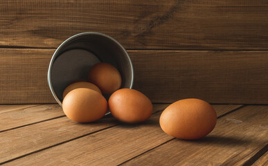Fresh eggs next to a small tin bucket, pail or metal container. Composition on wooden table.