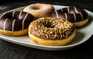 Delicious glazed doughnuts on a white plate. Assorted donuts with chocolate frost and sprinkles.