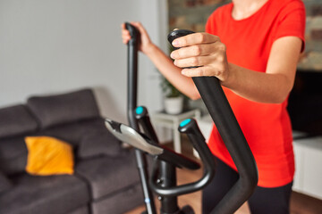 Unrecognizable woman training at home using the elliptical trainer - obrazy, fototapety, plakaty