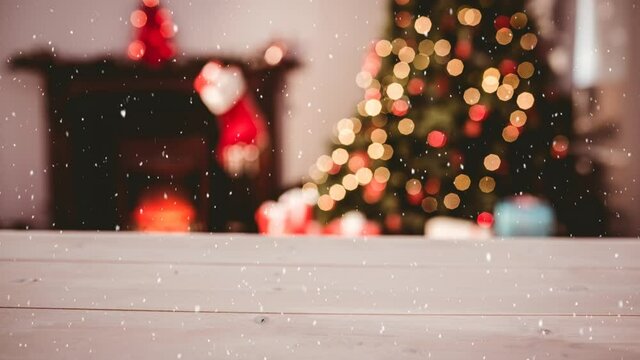 Animation of snow falling over blurred room and christmas decoration