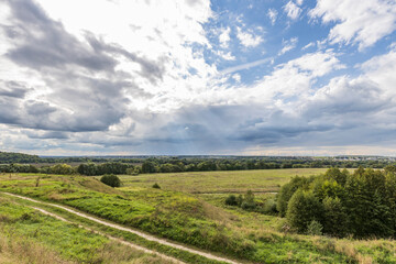 Naklejka premium Road through fields. Country road in summer field and clouds on blue sky.