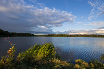 Cloudy sky over the river in the evening. Picturesque landscape with clouds and a river. Bright green grass in the foreground.