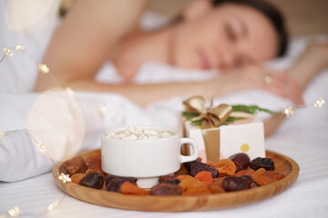 Woman sleeping on the bed with present and coffee with marshmallows standing near her. Mornig surprise
