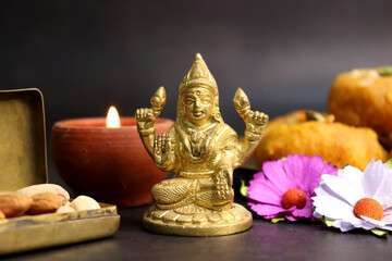 Beautiful diya, and Sweets with Golden statue of Goddess Laxmi on Laxmi pujan or pooja in Diwali or Deepavali, a festival of light. Navaratri Puja with flowers and dry fruits. Copy space.