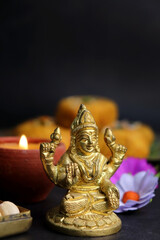 Beautiful diya, and Sweets with Golden statue of Goddess Laxmi on Laxmi pujan or pooja in Diwali or Deepavali, a festival of light. Navaratri Puja with flowers and dry fruits. Copy space.