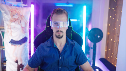 Attractive man geek portrait in gaming room with neon lights and dakimakura in background