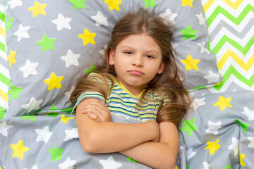 The child is lying in bed and is indignant, does not want to get up to go to school to study.