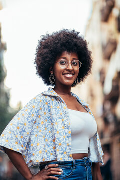 african woman on her 20s standing on the streets of Barcelona and looking at camera. she is posing with one hand on her hip and smiling