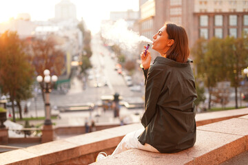 Woman at sunset with amazing city view, enjoying warm days, freedom, positive vibes, smoking ...