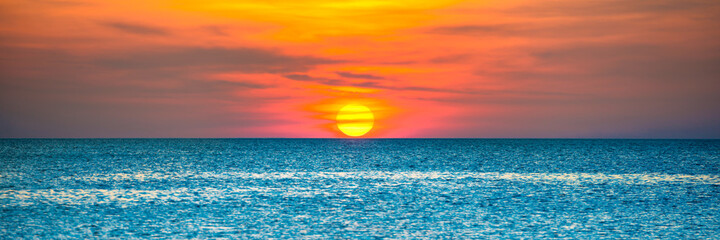 Panorama of nature landscape with beautiful dramatic orange sunset over blue rippled sea