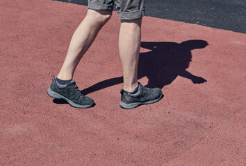The legs of a man in short shorts and black sneakers. Red and brownasphalt background. The concept of running and walking. Legs of young man in black sneakers. 