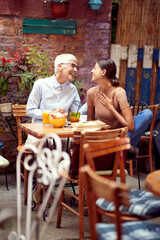 mother and adult young daughter sitting in outdoor cafe, looking each other, smiling.