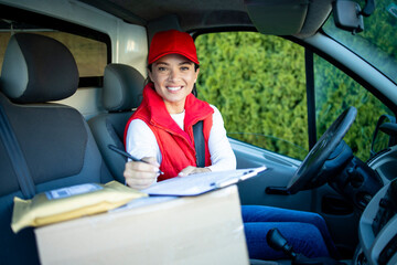 Portrait of beautiful female delivery worker or courier sitting in her van with parcels.