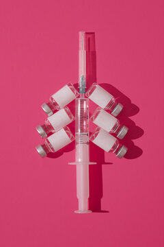 Syringe and vaccine bottles forming christmas tree against pink background. Minimal covid19 concept