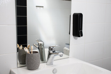 modern bathroom sink and faucet with black liquid soap and glass of toothbrushes 