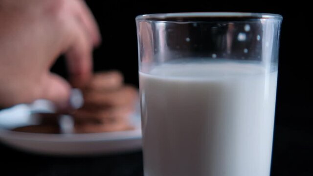 Hand dunking a cookie in glass of milk with black background