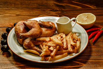 Grilled chicken legs with french fries, chips in plate with lemons and olives