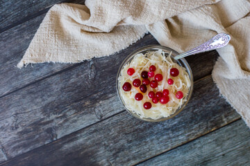 Sauerkraut with cranberries in glass bowl next to beige towel on wooden background, top view