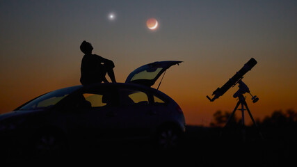 Silhouette of a man, telescope and countryside under the starry skies.