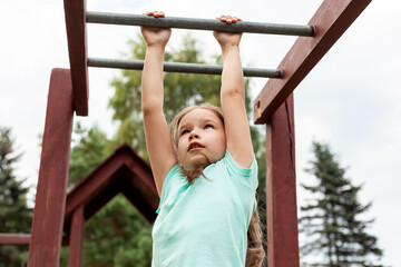 One active young girl, fit sporty child climbing, outdoor exercise, hanging on a bar on a playground, portrait, closeup. Children and healthy physical activities in summer simple concept, lifestyle